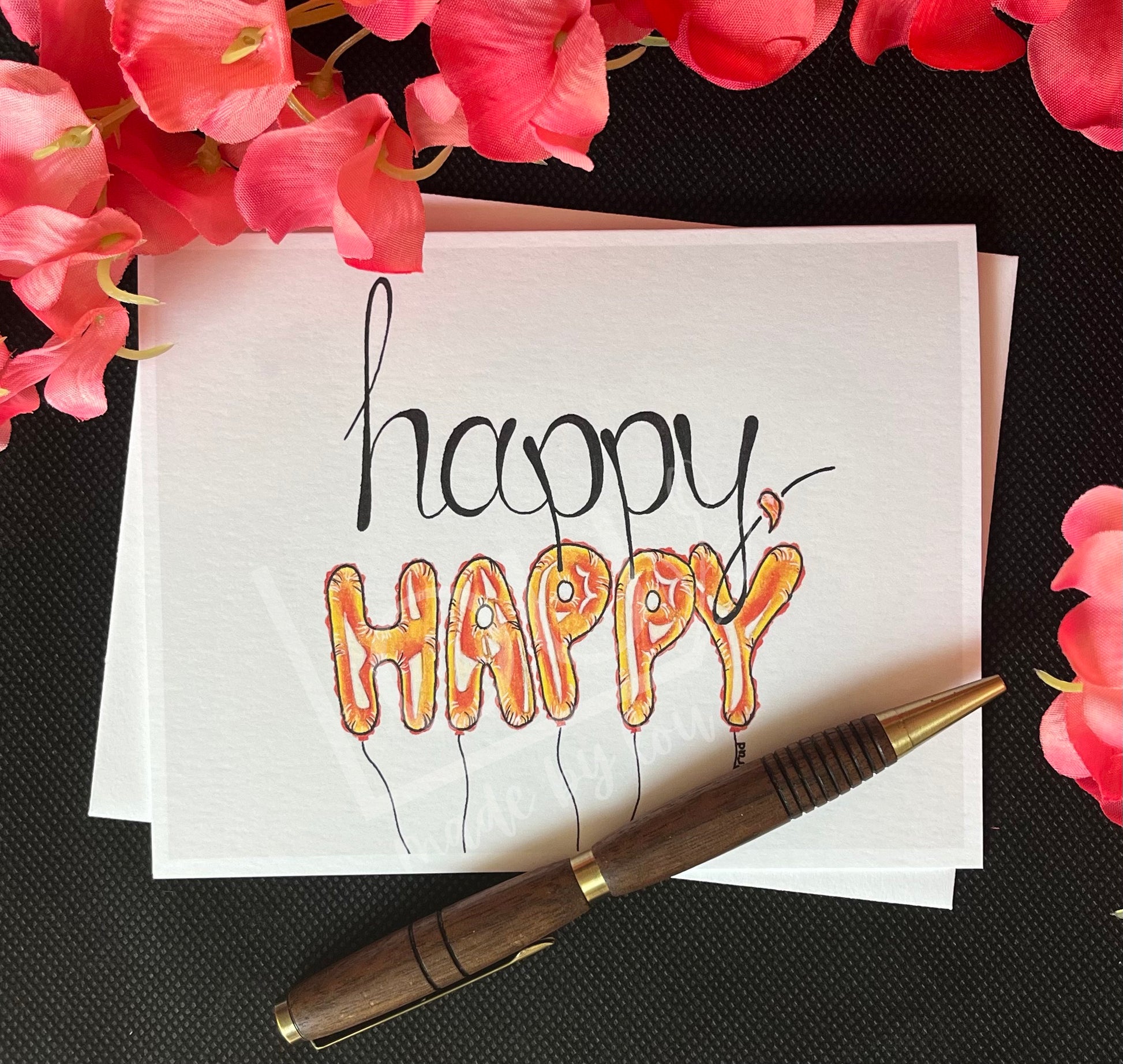 Card with 'happy happy' text, pen, and pink flowers on a black textured background