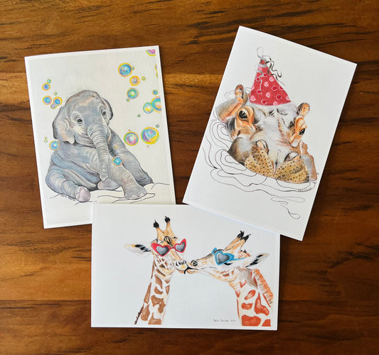 Three illustrated greeting cards featuring animals on a wooden surface.