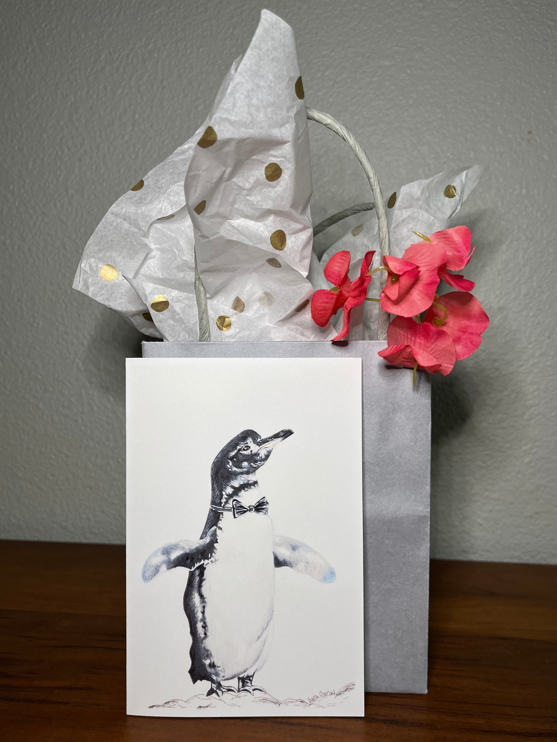 Penguin greeting card in front of a grey gift bag with polka dot tissue paper