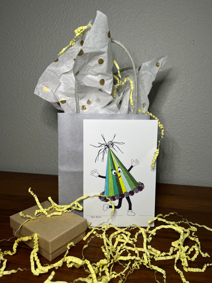 Gift bag with a card featuring a colorful character, surrounded by yellow paper shreds on a wooden surface.