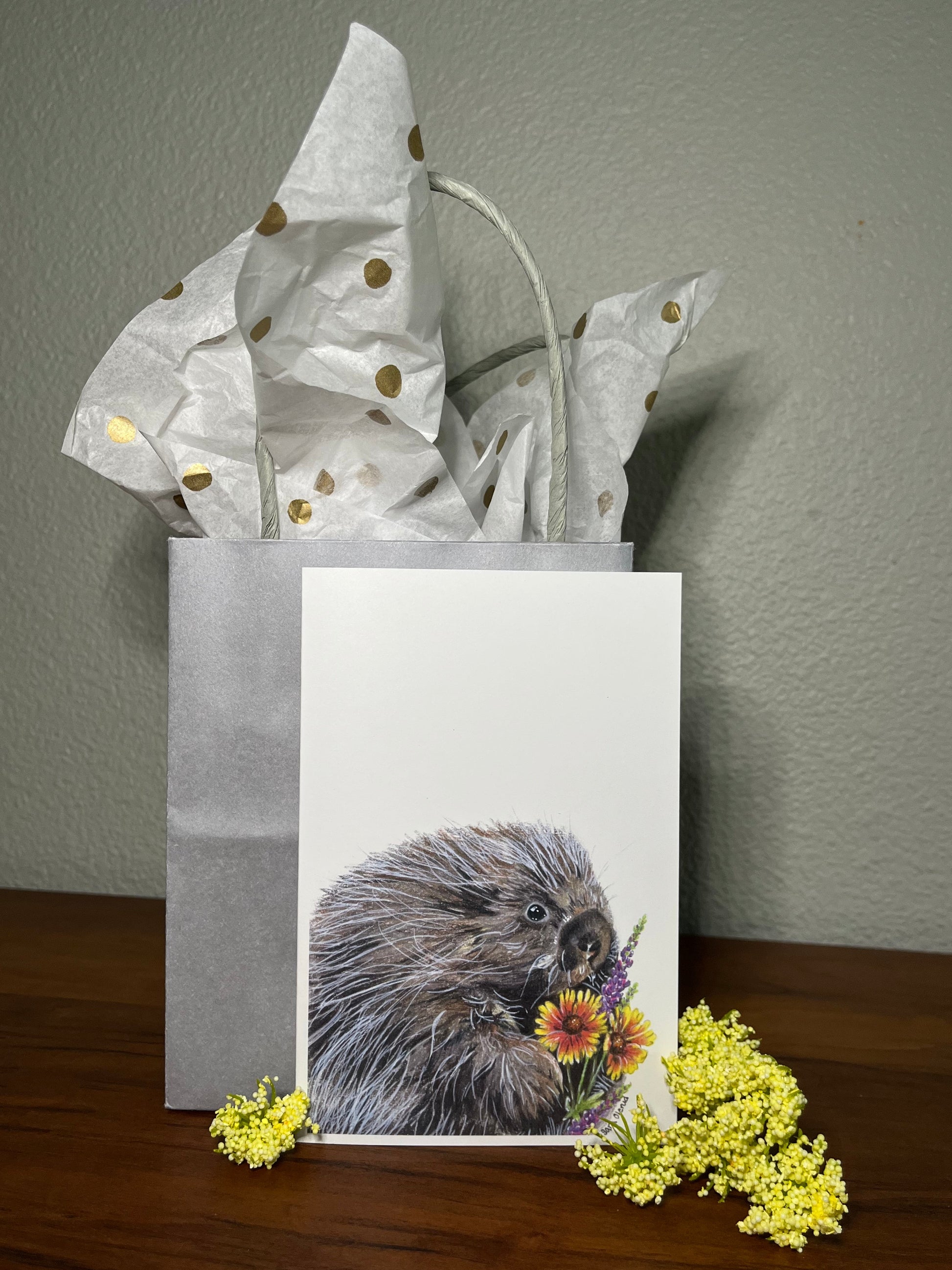 Gift bag with a beaver illustration and flowers on a wooden surface.