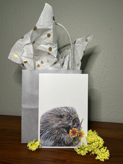 Gift bag with a beaver illustration and flowers on a wooden surface.