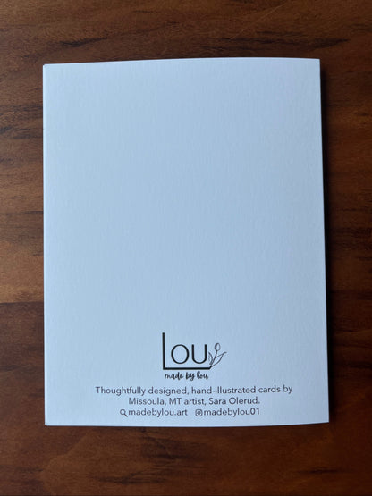 A white textured card with black printed text and logo at the bottom, placed on a dark brown wooden surface. The card is branded 'lou made by Lou'.