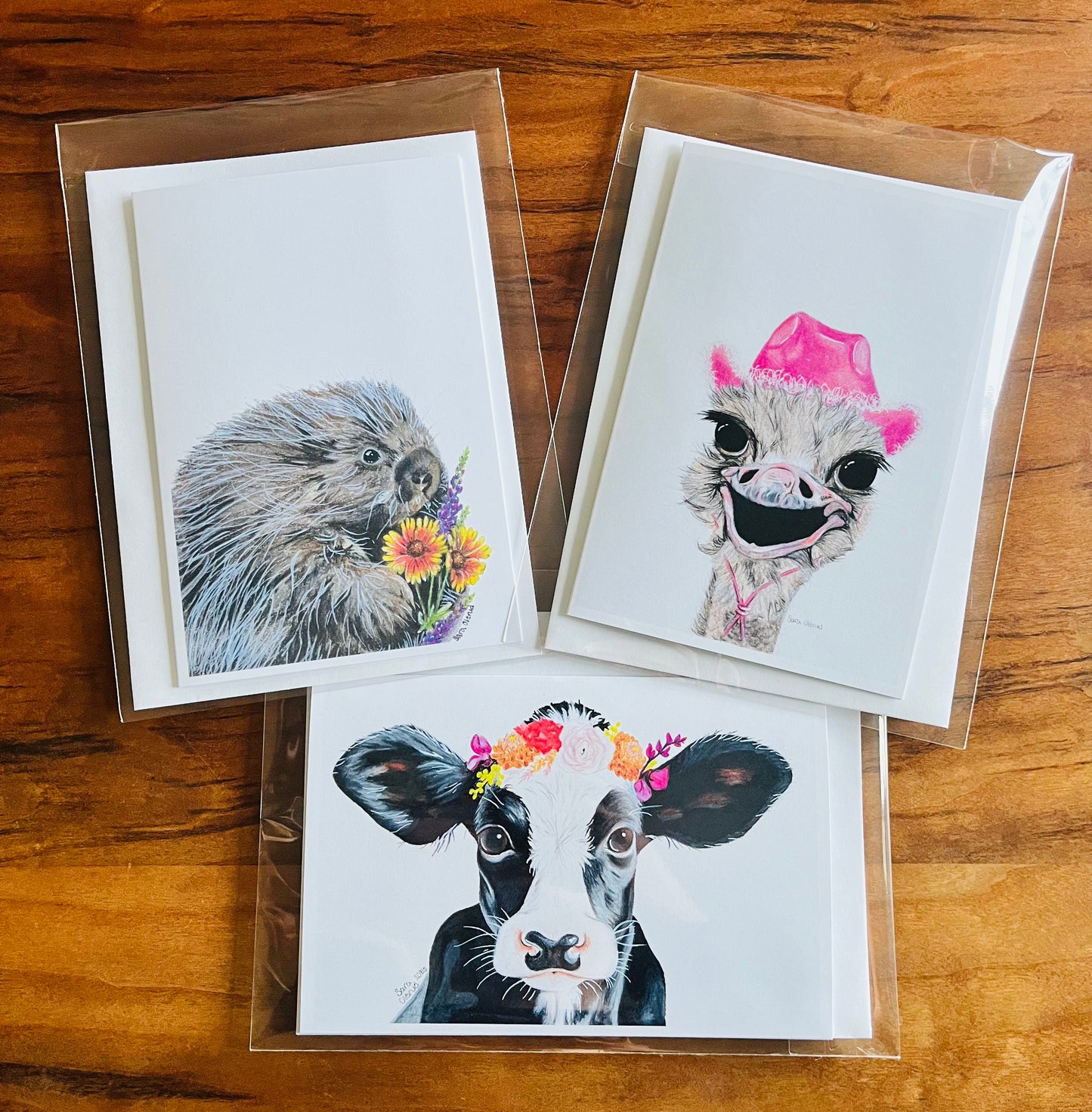 Three greeting cards with animal illustrations on a wooden surface