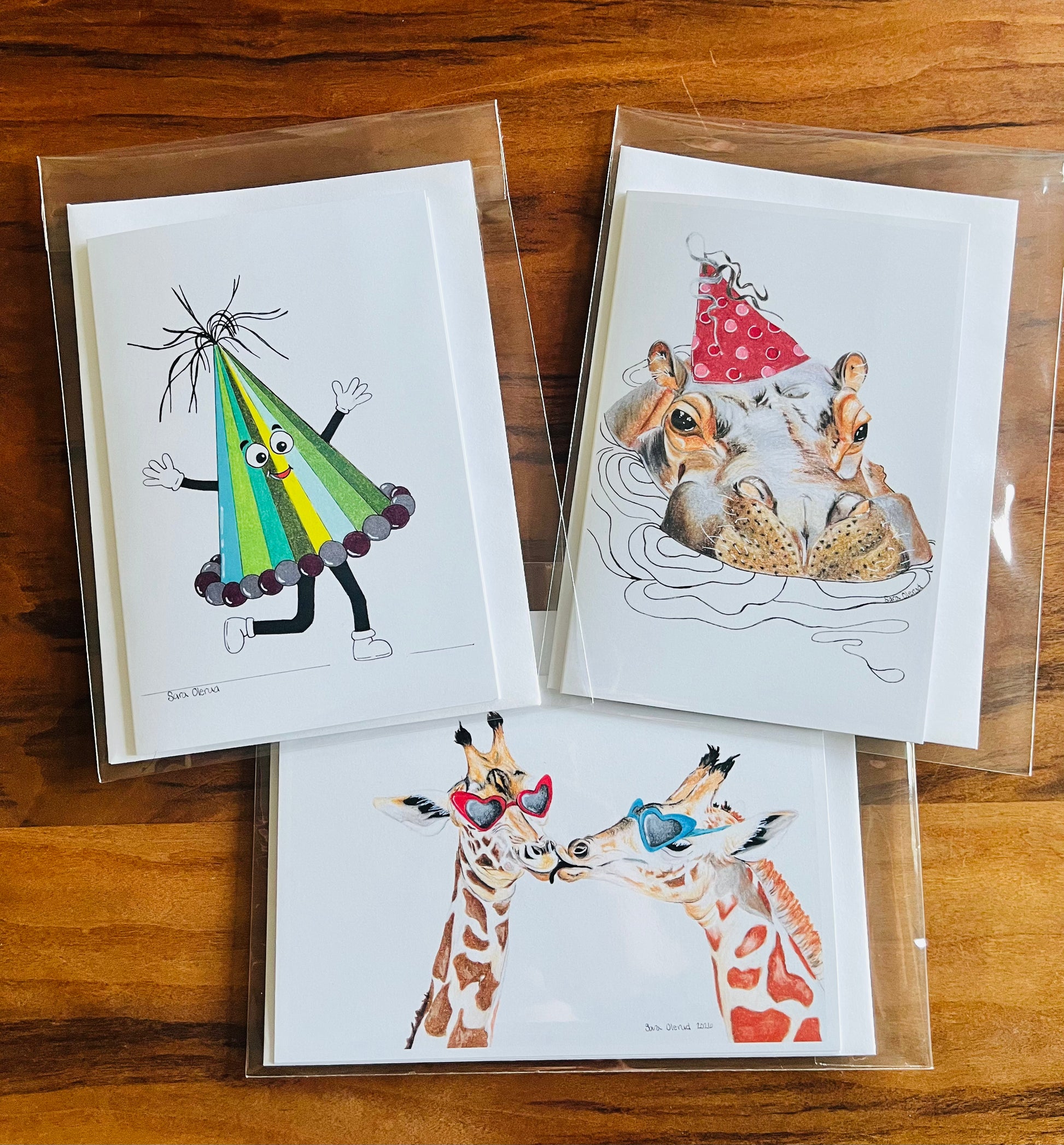 Three illustrated holiday greeting cards on a wooden surface