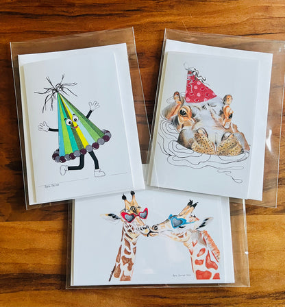 Three illustrated holiday greeting cards on a wooden surface