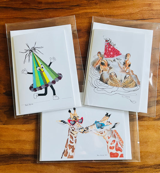 Three illustrated holiday greeting cards on a wooden surface